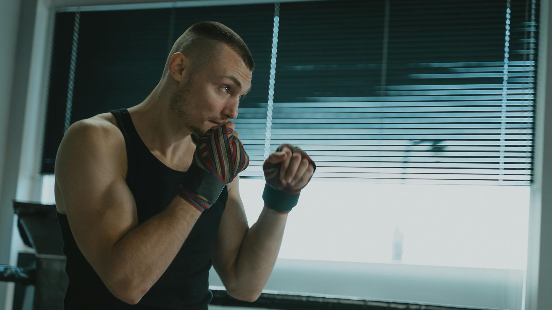 Man in a focused stance during a bodyweight exercise in a minimalist gym.
